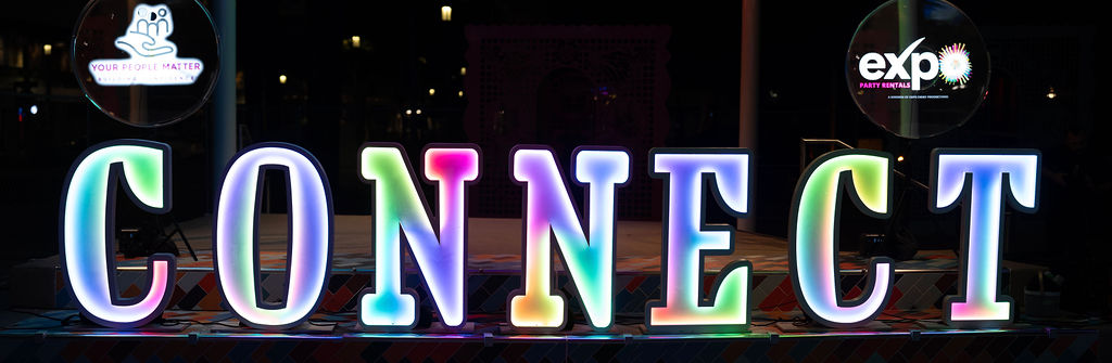Rainbow LED CONNECT letters flanked by two 3D hologram fans at night